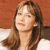 Static pixelated image of a person with long brown hair against an orange background, cropped to show upper body and face.