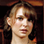 Pixelated close-up of a person with light brown hair and fair skin, wearing a dark top against a dark background.
