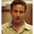 Static pixelated image of a man with short dark hair wearing a light-colored collared shirt against a blurred indoor background.