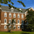 Pixelated image of a multi-story brick building with white-trimmed windows, gray roof, and green trees under a blue sky.