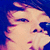 A person with dark hair and light skin holds a microphone close to their mouth, captured in a pixelated image.