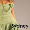 A cropped image shows a person in a light green dress with a floral necklace and fringed skirt, with the name 'Sydney' in black text at the bottom right.