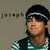 A pixelated image of a person wearing a dark cap with white stripes, striped shirt, and vest against a gray background with repeated text.