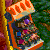 Pixelated image of a cartoon character with orange hair and blue clothing riding a roller coaster, set against green foliage background.