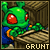 Green cartoon character with red eyes and antennae, wearing blue outfit with orange accents, leaning on wooden structure beneath text.