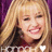 Pixelated close-up of a smiling person with long blonde hair against a purple background, wearing a dark top with a white star-like shape.