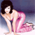 Pixelated image of a woman with dark hair in a pink dress, kneeling on a light surface against a gradient background.