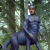 Pixelated figure in blue attire stands against blurred green foliage background with light streaks, head slightly tilted, one arm extended.