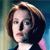 Pixelated portrait of a person with light brown hair styled in a bob, wearing a dark top with a white collar and pink shoulder detail against a blurred background.