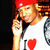 Pixelated image of a person wearing a red cap, white shirt with 'I ❤️' text, holding a microphone, and displaying a raised hand gesture.