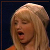 A static image of a person with long blonde hair wearing a light-colored head covering, mouth open in a shout or yell, against a dark blue background with an orange dotted border.