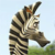 Pixelated image of a striped animal with a long neck and head raised against a light blue sky and green ground.