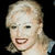 Pixelated static image of a person with light-colored hair and visible facial features against dark background.