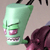 Green cartoon character with large head, pink mouth, and visible teeth, wearing dark purple clothing with pink accents, positioned against light gray background.