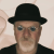 Pixelated image of a person wearing a black bowler hat and dark clothing against a light background.