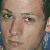 Static close-up of a person's face with light skin tone, visible eyes, nose, mouth, and dark hair on the right side, against a blurred background with blue and white tones.