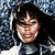 A pixelated close-up of a person with dark hair and a light-colored top against a blue and white patterned background.