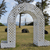 Pixelated static image of a stone archway with three openings, set against a grassy field and blue sky with scattered clouds.