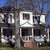 Pixelated static image of a two-story house with dark roof, white trim, and brown accents under a blue sky.