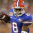 Pixelated image of a football player in blue uniform with white number 8, orange helmet, and brown football, standing against blurred background.