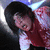 Pixelated image of a person with dark hair wearing a red jacket over a white shirt, leaning forward against a blurred background.