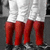 Three figures in white shorts and red socks stand side-by-side, viewed from the waist down against a gray background.