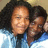 Two people in blue shirts pose closely together with one person's arm around the other, set against a light background.