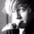 Black-and-white pixelated static image of a person's face with visible hair and clothing details, rendered in grayscale tones on a transparent background.