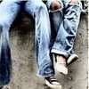 Close-up of two people's legs in light blue denim jeans with knee holes, one wearing black and white sneakers, the other in white shoes, on a textured ground surface.
