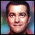Pixelated portrait of a person with short dark hair, light skin, and a neutral expression against a multicolored gradient background.