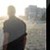 Pixelated static image of a figure in dark clothing standing against a light background with indistinct shapes.