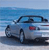 Pixelated static image of a light blue sedan with dark trim parked on a beach, facing left, against a blue sky and ocean background.