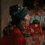 A person in a red garment holds a gray object with visible text, transitioning from a side view to a front view with a head tilt.
