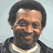 Pixelated image of a smiling person with short dark hair wearing a dark jacket over a light shirt, alongside blue text reading "Pudding Pop ?" and "Original Icons .com" on black backgrounds.