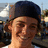 Pixelated close-up of a person with light skin wearing dark blue headwear, set against an indistinct outdoor background.