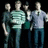 Four pixelated figures stand side-by-side against a black background, wearing casual clothing in muted tones.