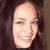 A static pixelated image shows a person with long dark hair, light skin, and a smiling expression, cropped to show the head and upper shoulders against a dark background.