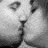 Black-and-white pixelated image of two faces in close proximity with visible eyes, nose, and mouth areas suggesting a kissing gesture on a gray background.