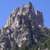 Pixelated mountain landscape with rocky peaks under clear blue sky, green foliage at base, no visible text or human figures.