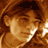 Pixelated static image of a person's face with brown hair and light skin tone, rendered in warm orange-brown color palette on transparent background.