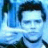 Pixelated blue-toned image of a person with dark hair and light skin, wearing a dark shirt against a blurred background.