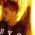 A pixelated image of a person with long blonde hair wearing a dark shirt with white text, shown in two with slight head movement