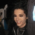 Pixelated static image of a person with dark hair wearing a black top, positioned against a dark background with light and blue elements on the left.