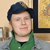 Static pixelated image of a person wearing a dark blue beret and green shirt against an indoor background with framed artwork.