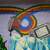 Animated rainbow swirl with central white circle, blue waterfalls below, and gray rectangular shapes on the right side.