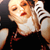 A pixelated image of a person with light skin and red lips, wearing a black top with white accents, holding a striped object near their face.