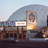 Pixelated static image of a theater facade with a marquee, framed poster, and architectural details under a light sky.