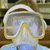 A person wearing a diving mask with yellow trim and white straps, blue shirt visible beneath.
