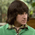 Pixelated image of a person with dark brown hair wearing a green top against a blurred background with green and brown tones.