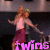 Pixelated static image of two figures in motion, one with light hair and pink top, the other with darker hair and gray top, against dark background with purple text.